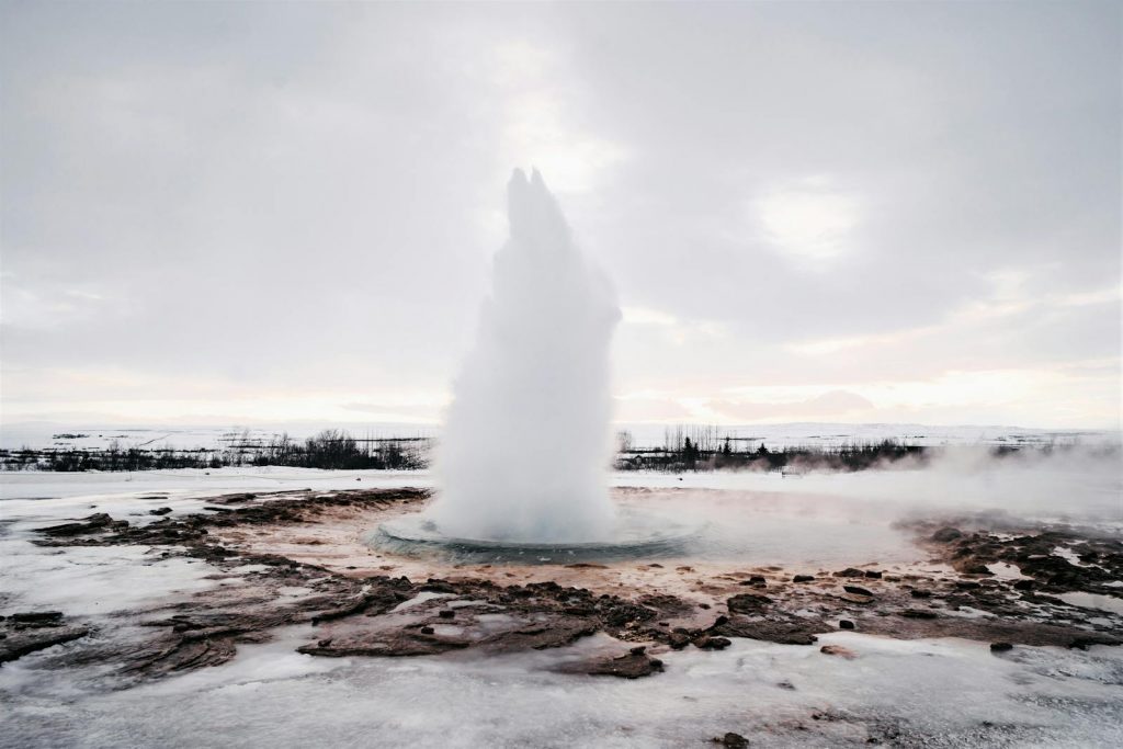 Captivating view of Strokkur geyser erupting against a snowy Icelandic backdrop in winter.