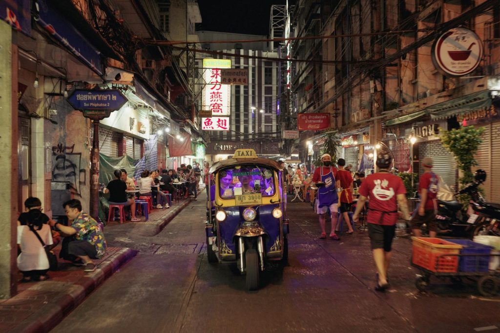 Vibrant night street scene featuring an auto rickshaw in a busy city alley.
