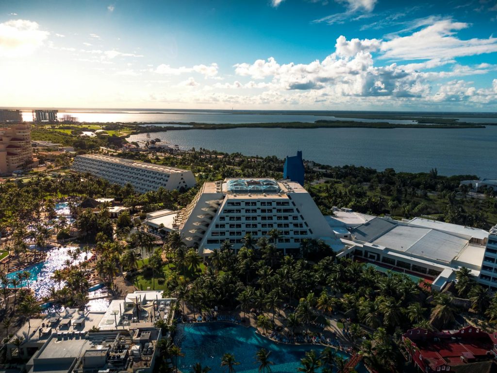 Stunning aerial view of a tropical beachfront resort in Cancun, Mexico, featuring lush palm trees and blue waters.