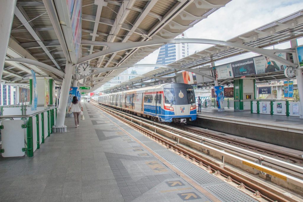 A bustling urban railway station with a modern train and commuters in daylight.