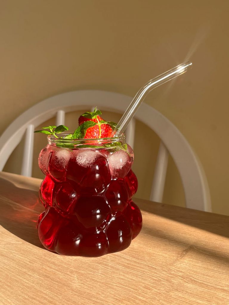 Stylish glass with a refreshing hibiscus and peppermint drink, garnished with strawberries.