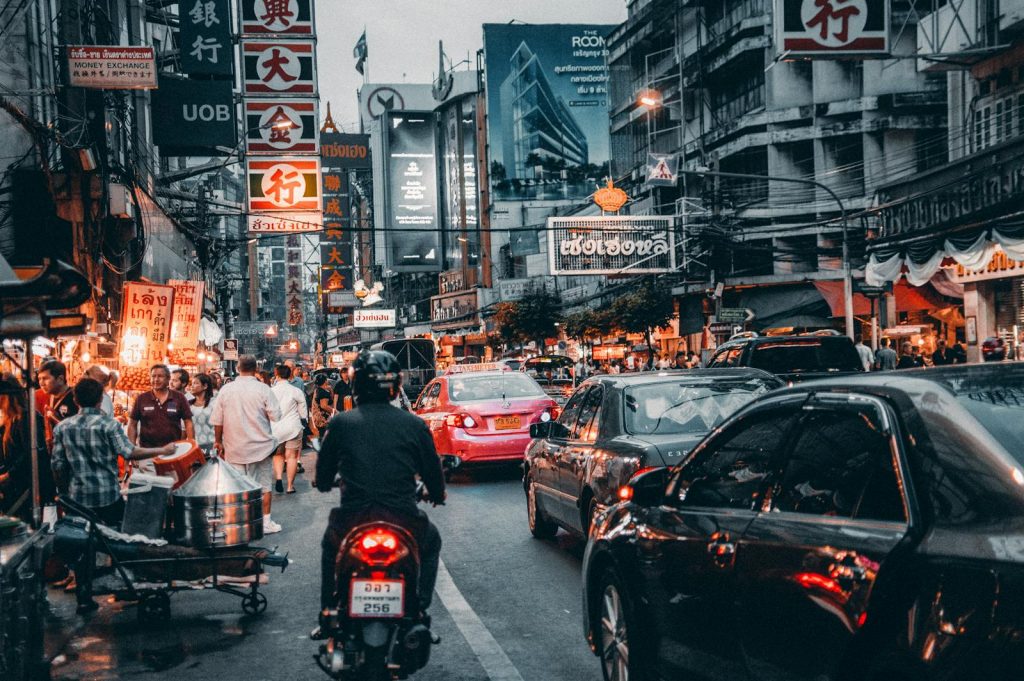 Dynamic scene of busy street life in Bangkok's Chinatown at night with cars and bustling crowds.
