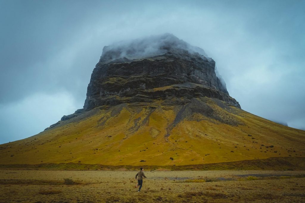 A lone runner traverses scenic Iceland with a dramatic rocky mountain and moody skies.