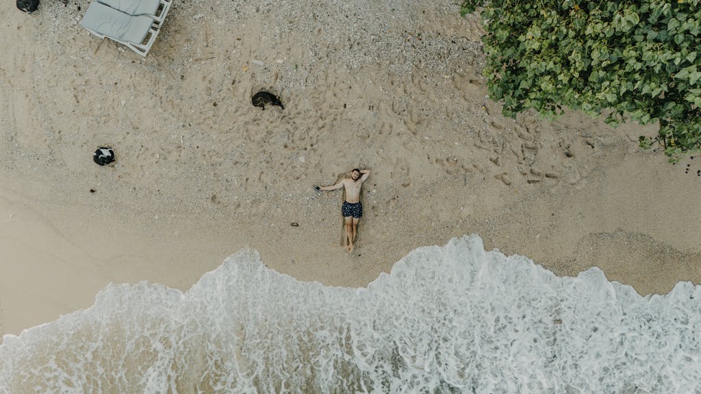 A tranquil aerial shot captures a person resting on a sandy beach by the ocean in Sri Lanka.