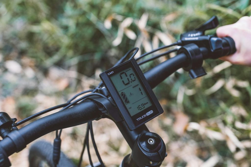 A detailed view of bicycle handlebars with a digital screen in an autumn setting.