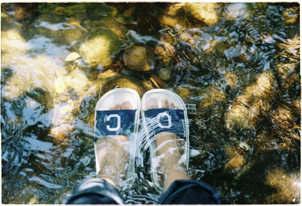 A close-up of feet in flip flops standing in a clear stream.