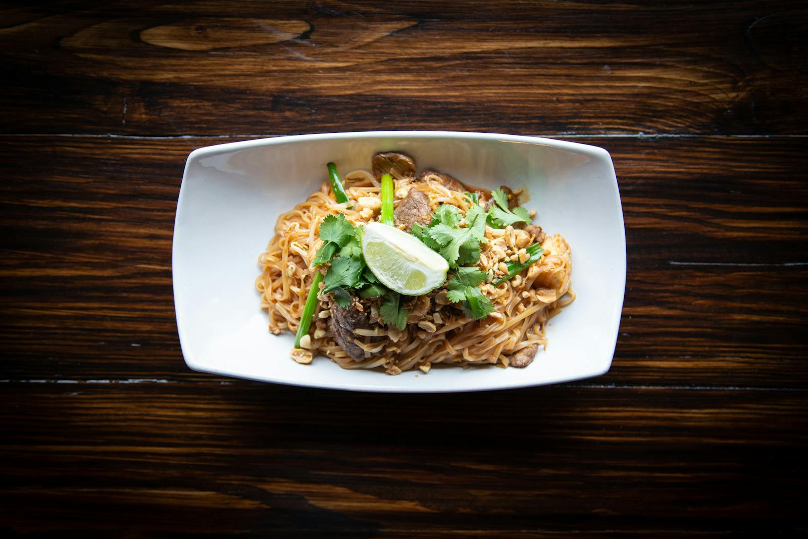 Delicious Pad Thai noodles served with lime and cilantro on a wooden table.