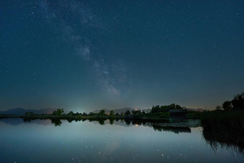 A serene night sky over Chiemsee, Germany, featuring stars and lake reflections.