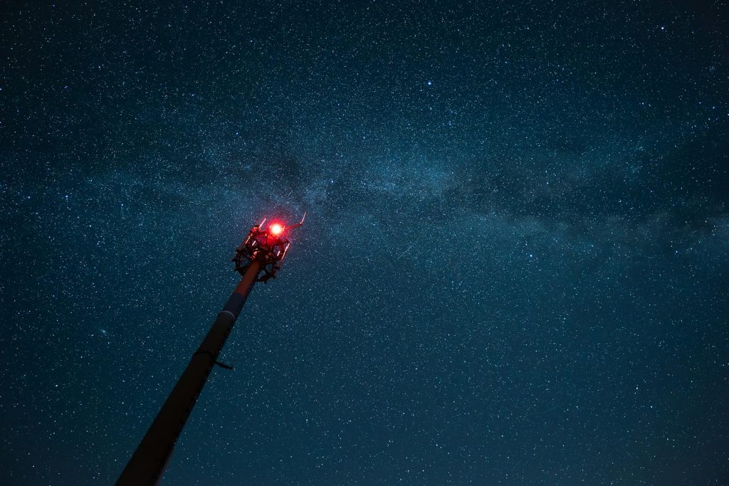 A relay tower with red warning lights under the starry night sky in Gersfeld, Germany.