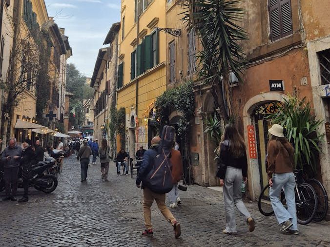 Cobblestone street bustling with life in Trastevere, Rome, showcasing historic architecture.