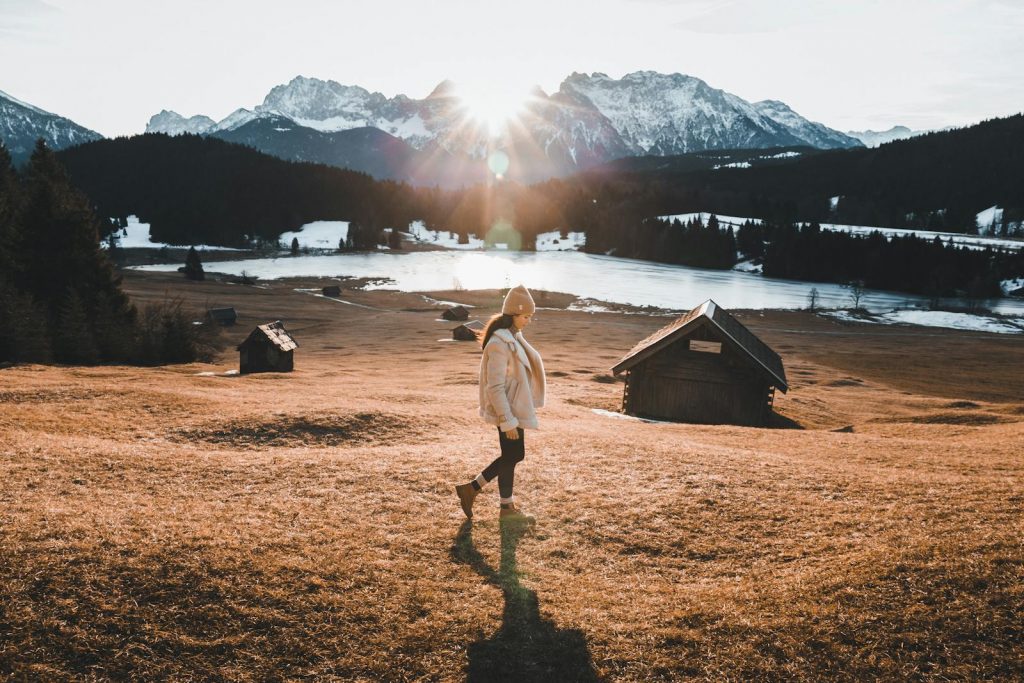 Young woman walking in winter sunlight across a Bavarian field with mountain backdrop.