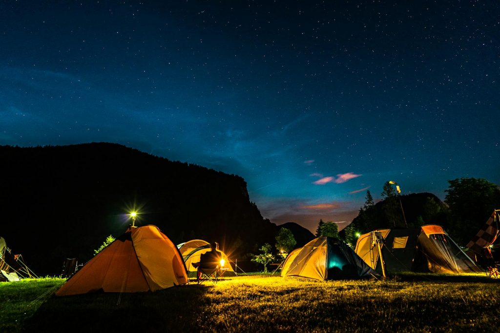 A serene camping site under a starry night sky with glowing tents and mountains.