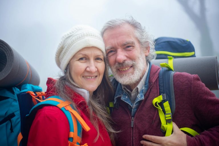 Senior couple hiking with backpacks, smiling in the outdoor misty environment of Portugal.