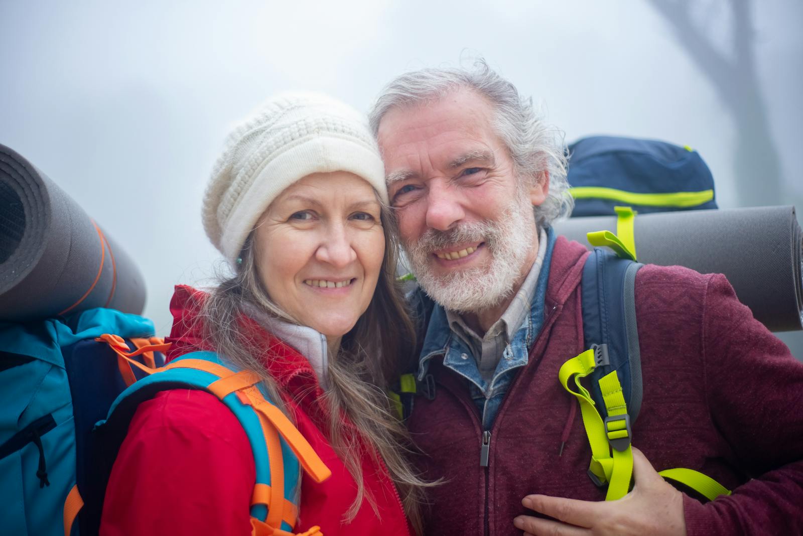 Senior couple hiking with backpacks, smiling in the outdoor misty environment of Portugal.