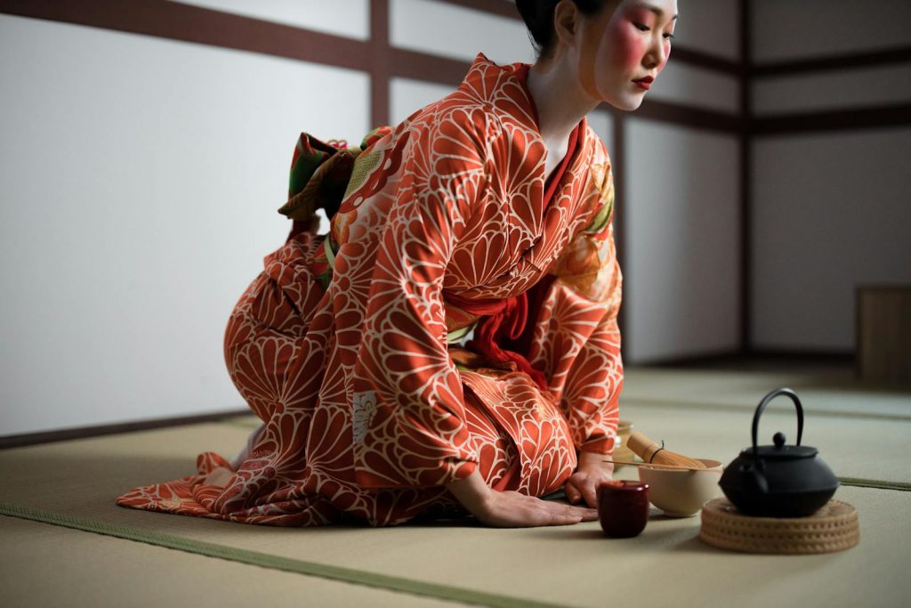 A woman in a vibrant kimono participates in a traditional Japanese tea ceremony indoors.