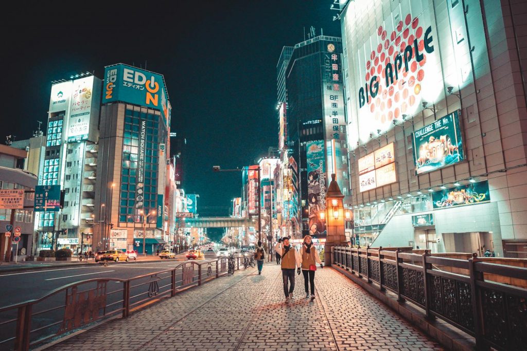 Urban Japan cityscape at night with illuminated buildings and people walking along the street.