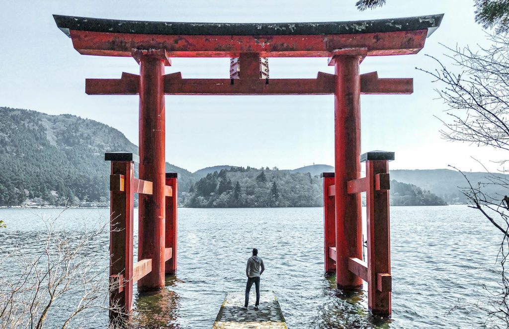 A person stands at Hakone Shrine's iconic torii gate on Lake Ashi, Japan, offering a tranquil view.