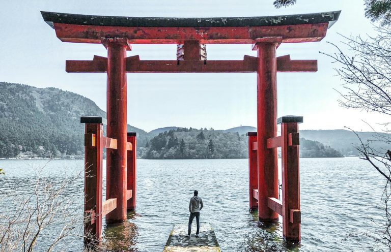 A person stands at Hakone Shrine's iconic torii gate on Lake Ashi, Japan, offering a tranquil view.