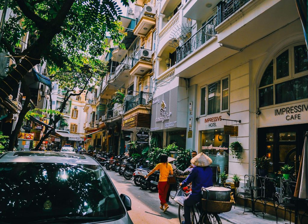 Vibrant street life in Hanoi with locals, cafes, and motorbikes on a sunny day.
