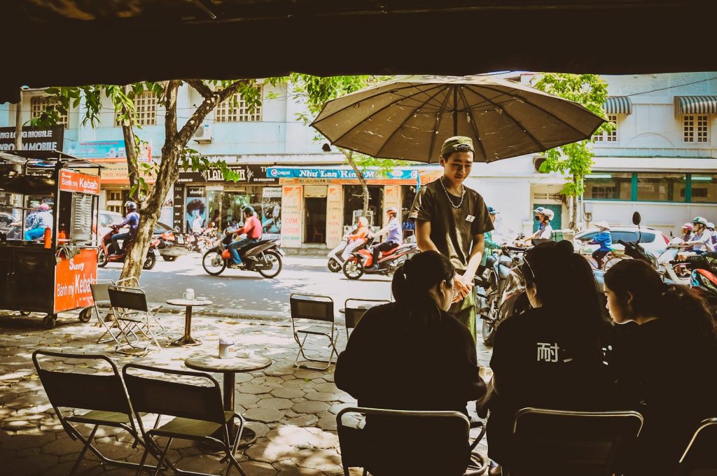 A bustling street cafe in Hanoi, Vietnam captures the lively atmosphere with people dining outdoors.