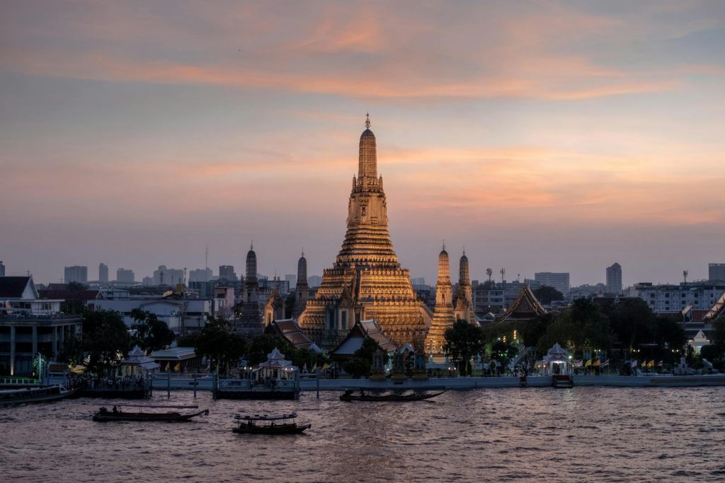 Beautiful view of Wat Arun temple by the river in Bangkok during sunset.