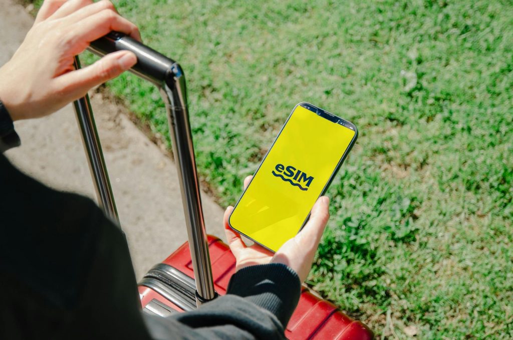 A person holds a smartphone showing an eSIM app while standing with luggage outdoors in Los Angeles.