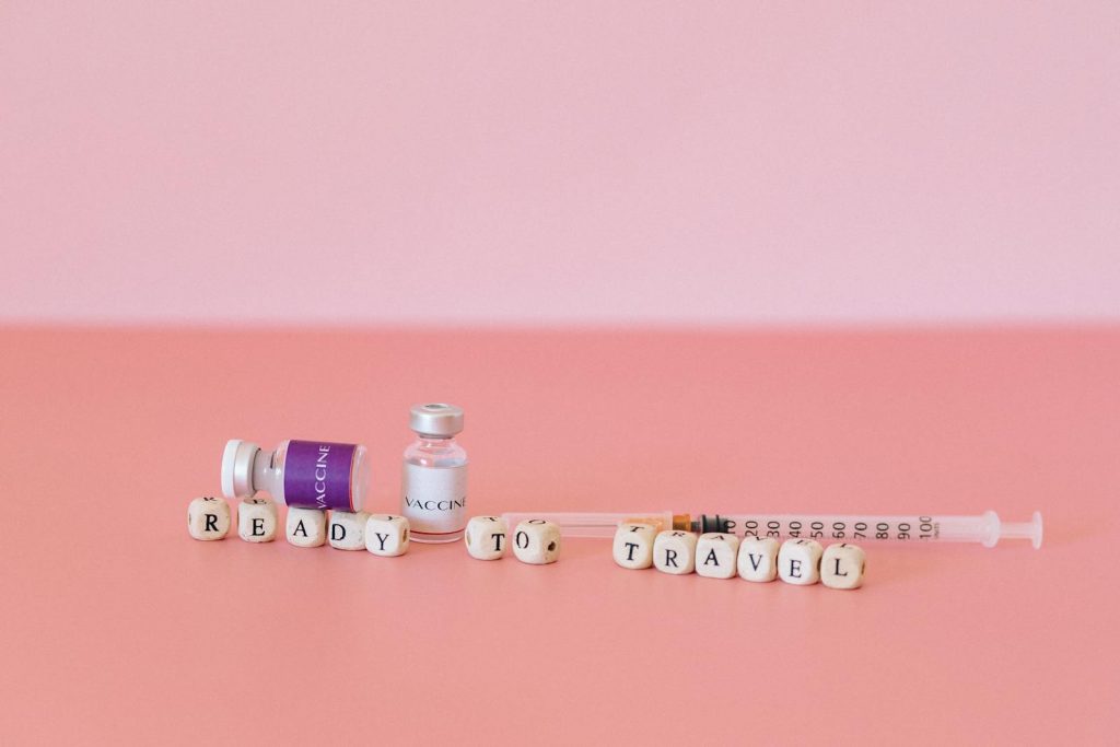 Close-up of vaccine vials, syringe, and the words 'Ready to Travel' on a pink background.