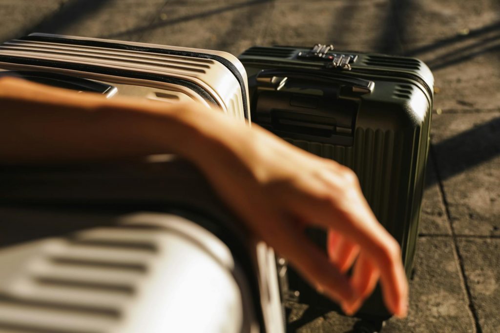 Photograph of a person's hand resting on luggage under sunlight on pavement.