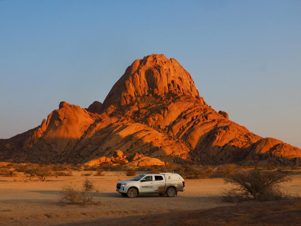 Dramatic sunset over Spitzkoppe, Namibia with a car in the foreground.