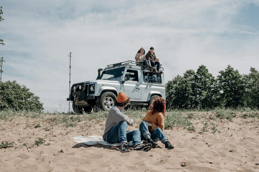 Group of friends enjoying leisure time outdoors with SUV on sandy terrain.