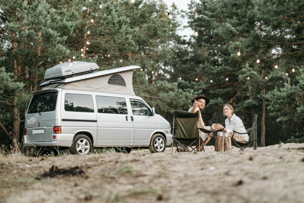 Happy couple camping outdoors with van and scenic nature backdrop.