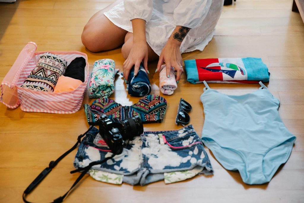 Person preparing for beach trip with essentials like clothes, camera, and towel.
