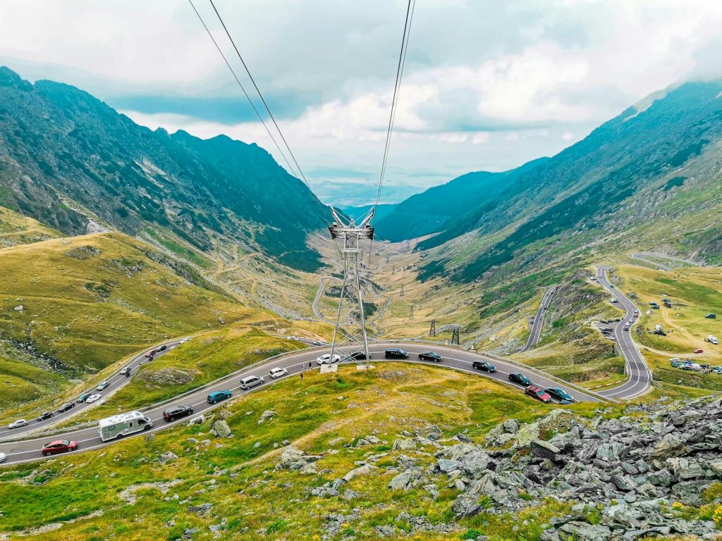 A breathtaking view of winding roads through a lush mountain valley with dramatic skies.