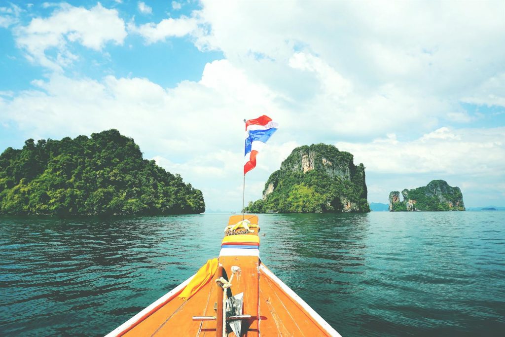 Long-tail boat sailing towards lush islands in the Andaman Sea on a sunny day.