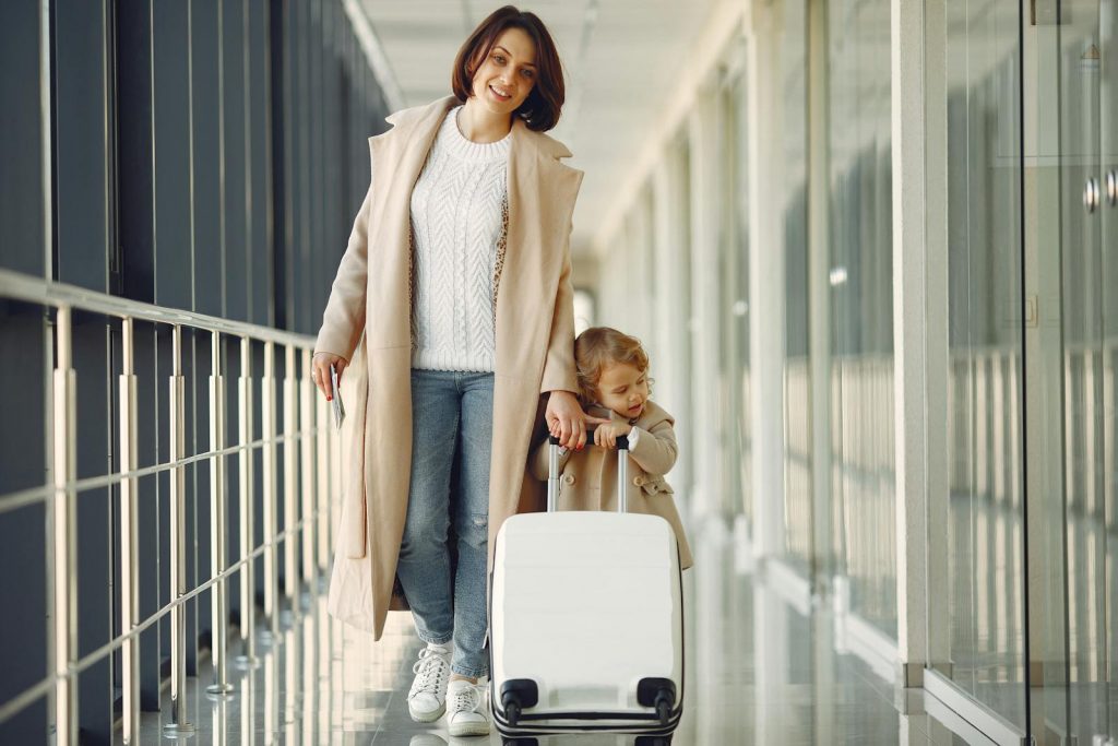 A mother and her daughter walking together in an airport terminal with luggage.