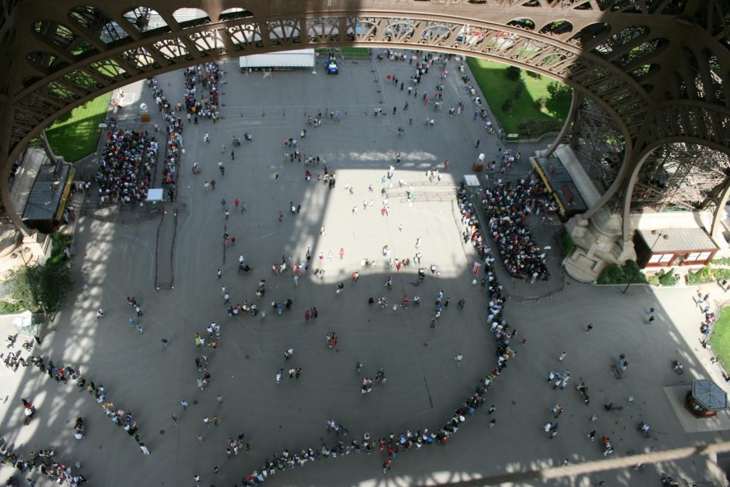 Overhead shot capturing long queues at the base of the Eiffel Tower in Paris, France.