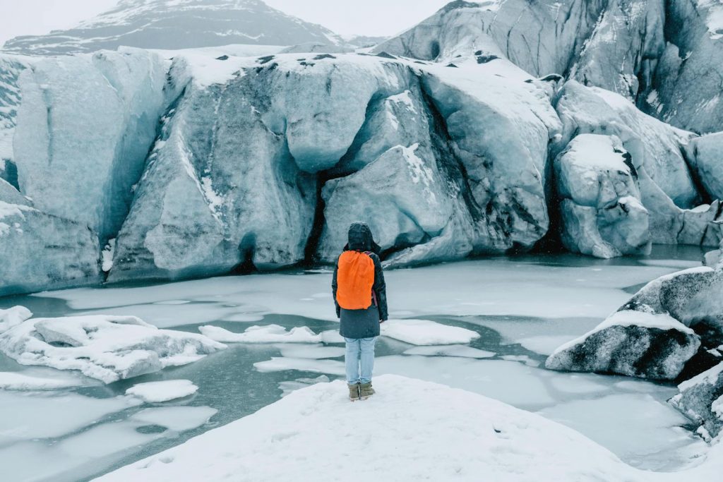 Person with backpack facing a massive glacier in Iceland, surrounded by ice and snow. Perfect for travel and adventure themes.
