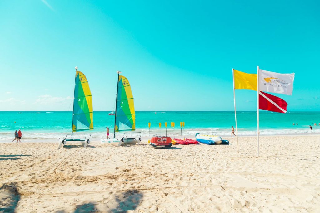 Bright summer day on Punta Cana beach with colorful sailboats and flags.