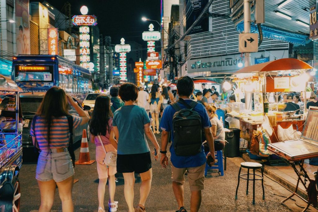 Vibrant night scene in an Asian city market with people exploring lively streets under neon lights.