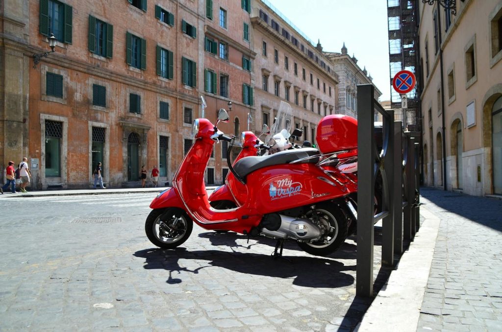 Vibrant red Vespa scooter parked on a sunny street in the heart of Rome, Italy.
