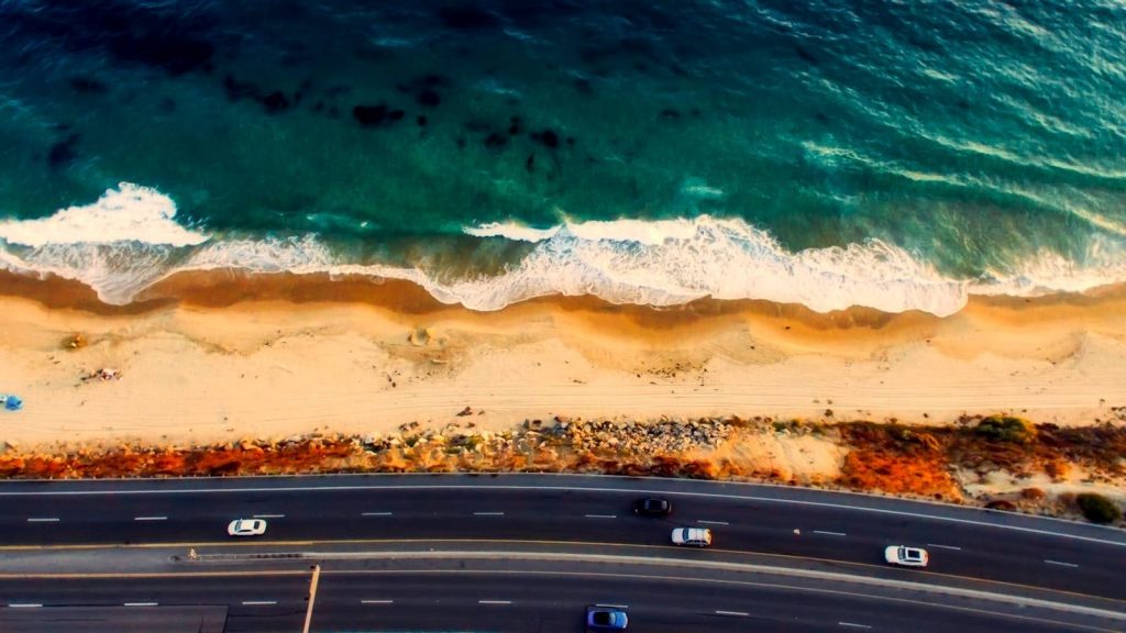 Stunning aerial view of a highway parallel to a tranquil beach and ocean waves.