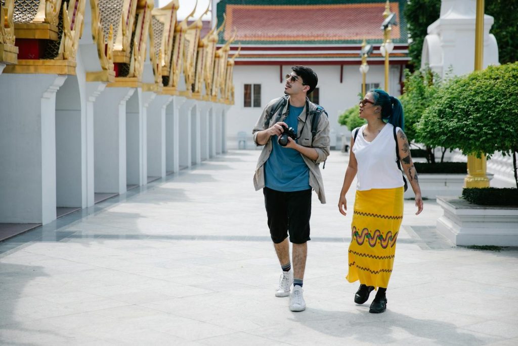 Two tourists walk and explore a traditional Thai temple, enjoying sightseeing and photography.
