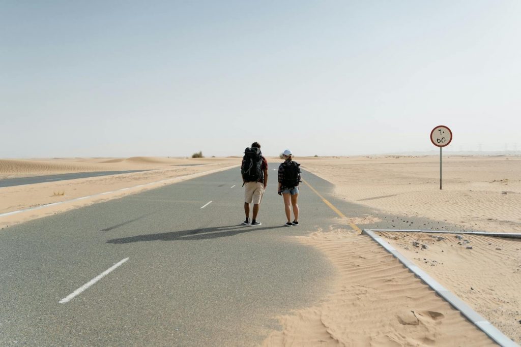Two backpackers hiking on a deserted road in a vast desert environment.