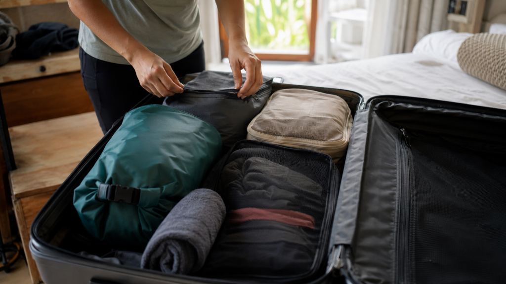 Reisender packt Packwürfel, Reisehandtuch und Drybag in einen Koffer