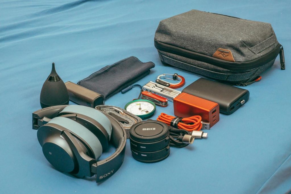 Flat Lay von Reiseausrüstung, darunter Kopfhörer, ein Kompass, eine Powerbank und Zubehör.