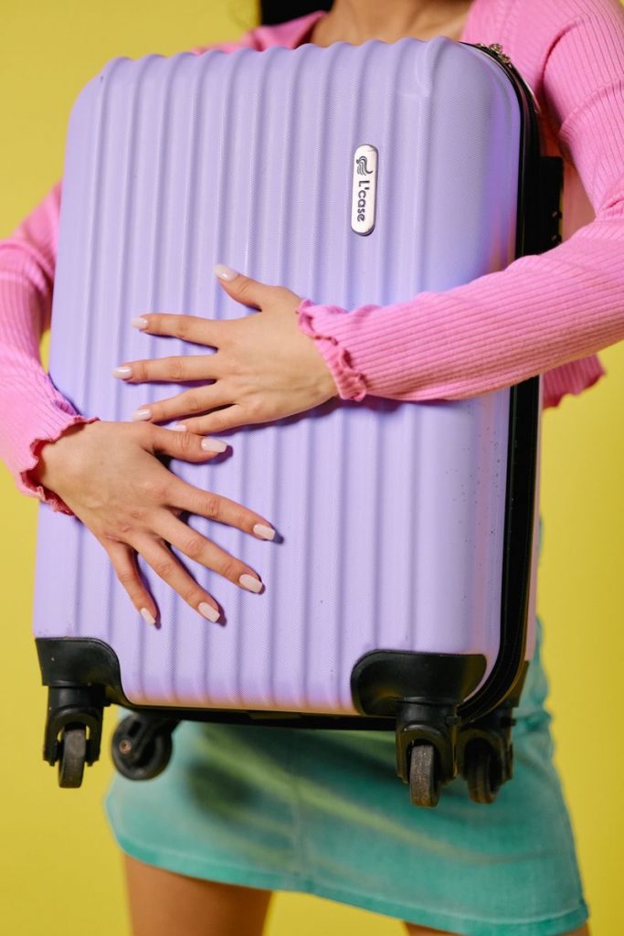 Stylish woman embraces a vibrant purple suitcase against a yellow background, showcasing travel fashion.