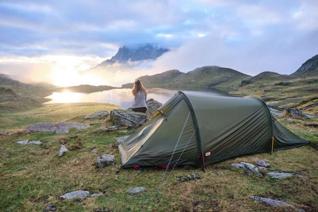 Serene camping scene with a woman by a tent, overlooking a lake at sunrise.