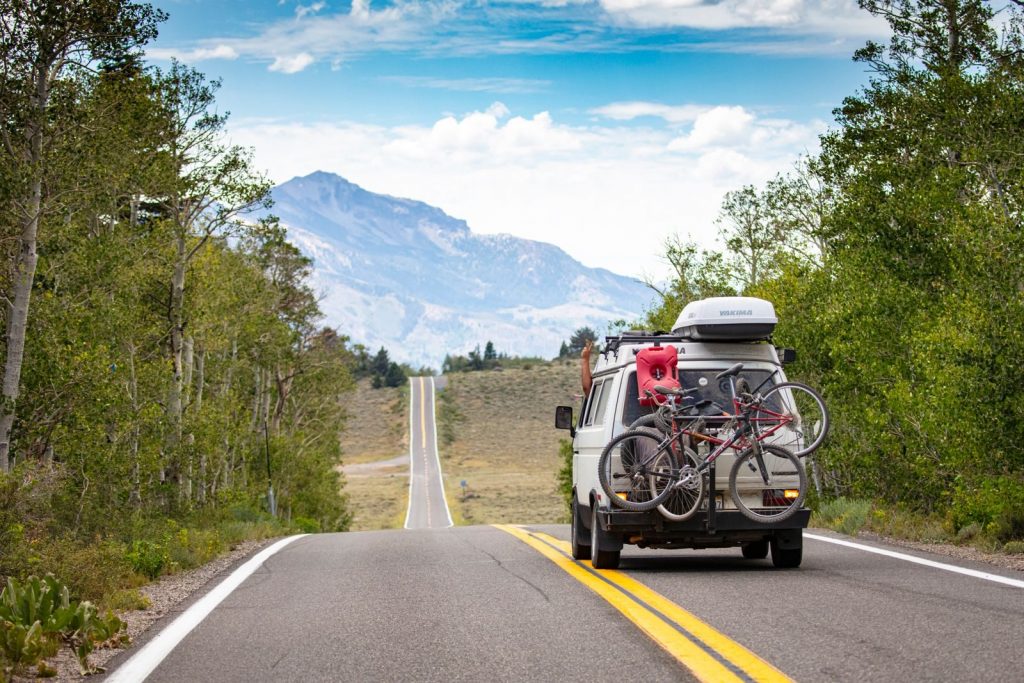 A camper van travels through a beautiful mountain landscape, bicycles mounted on the back.