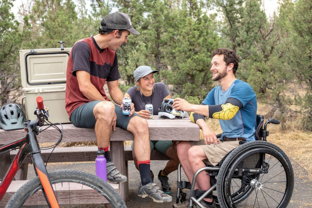 Group of friends having fun outdoors, chatting and enjoying drinks by a picnic table.