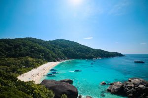 Scenic view of a tropical beach with clear blue waters and lush green hills, perfect for summer travel.